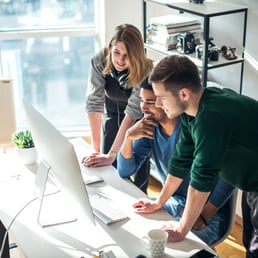 Small business owner and employees gathered around a computer screen