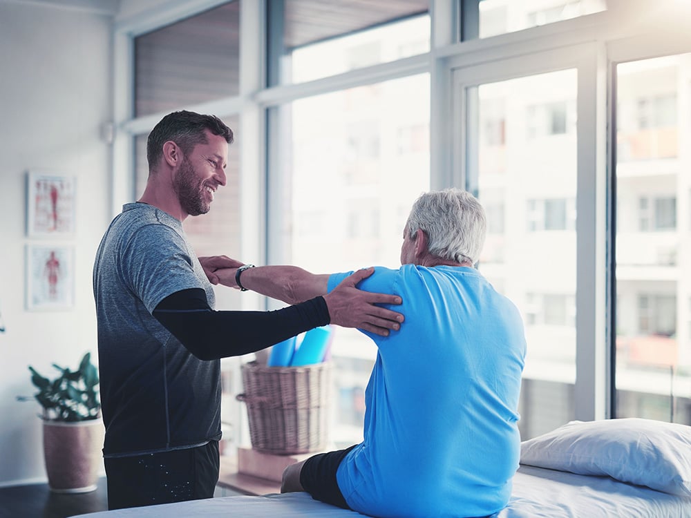 A business owner of a physical therapy office sretching a patient's shoulder 