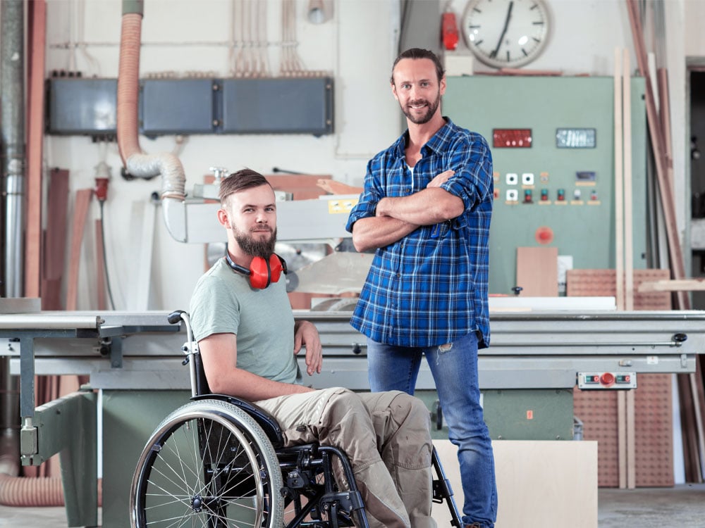 2 business owners of a woodworking shop in front of machinery. 