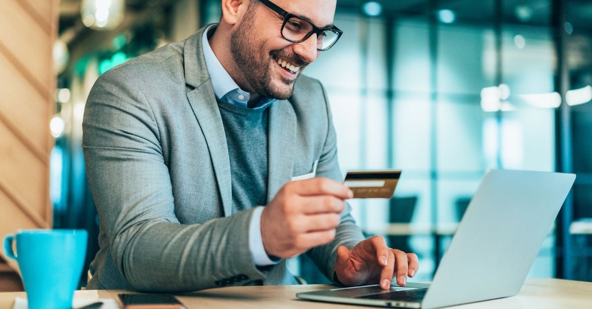 small business owner holding card smiling at laptop